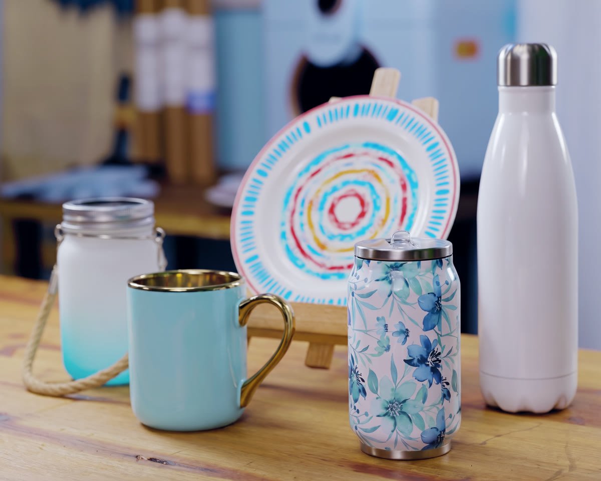 Caneca, garrafas, copo de vidro e prato sublimados sobre uma mesa de madeira